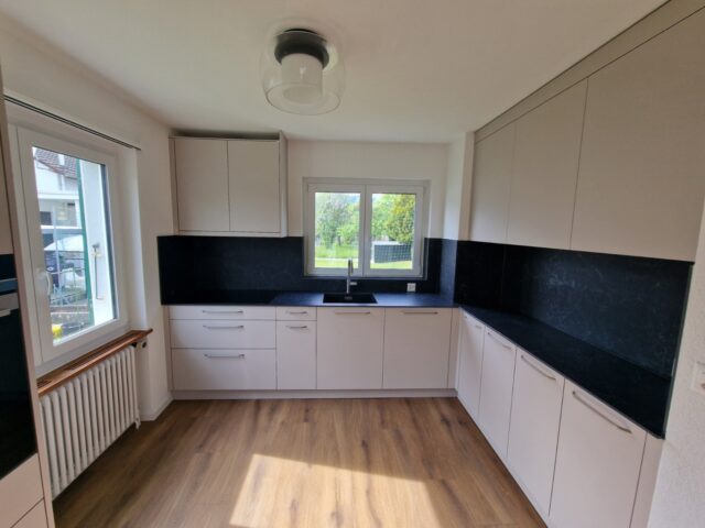 Helle Küche nach Mass in L-Form mit weissen Fronten und schwarzer Arbeitsplatte