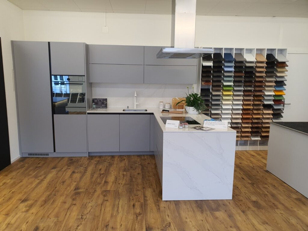Moderne Küche nach Mass in Ausstellung mit Kochinsel und Materialmustern