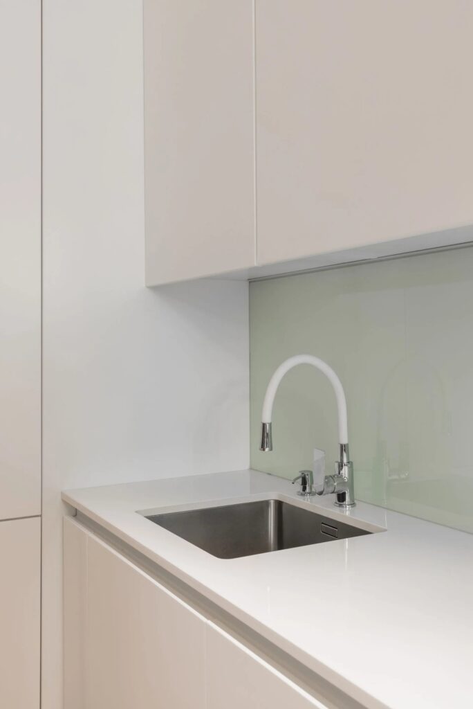 Modernes Spülbecken in einer Küche nach Mass mit weissen Fronten und Glasrückwand